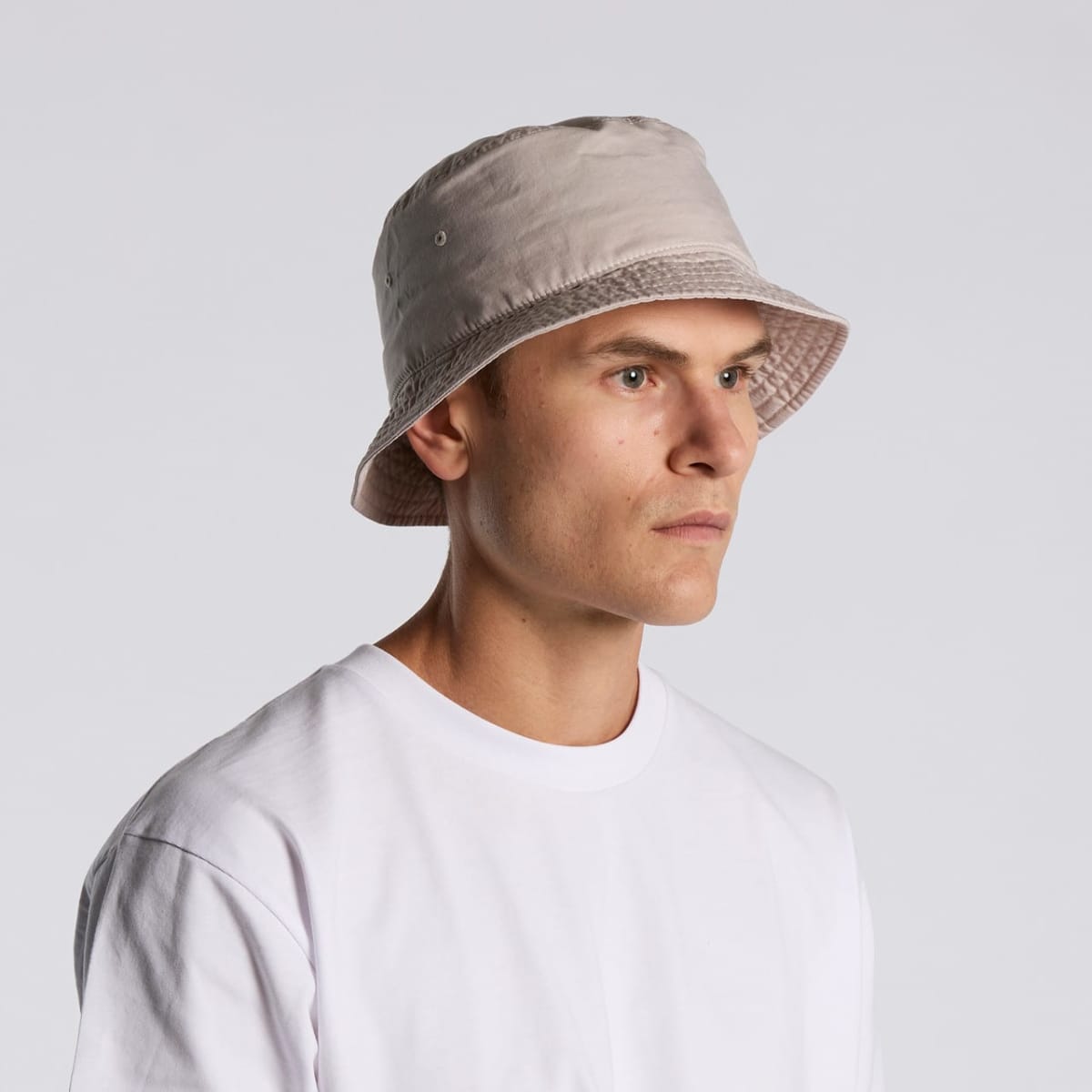 A person wearing a beige bucket hat and a plain white t-shirt, facing left.