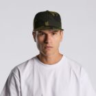Man in a white t-shirt and camo hat facing forward with a neutral expression.