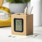 A pen holder with a digital clock and pens on a desk.