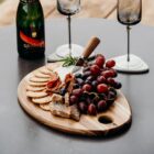 Charcuterie board with crackers, cheese, grapes, and wine on a table with two glasses.