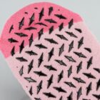Close-up of a pink sock with black rubber grip shapes on the bottom.