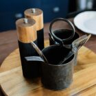 Salt and pepper grinders with forks and spoons in metal cups on a wooden tray.