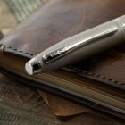 A silver Cross pen resting on a closed brown leather notebook.