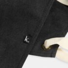 Close-up of a dark fabric with a k. tag and ivory-colored laces through metal eyelets.