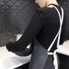 Person in a black shirt and apron holding a metal mixing bowl in a modern kitchen.