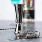 A metal jigger and cocktail strainer on a countertop.