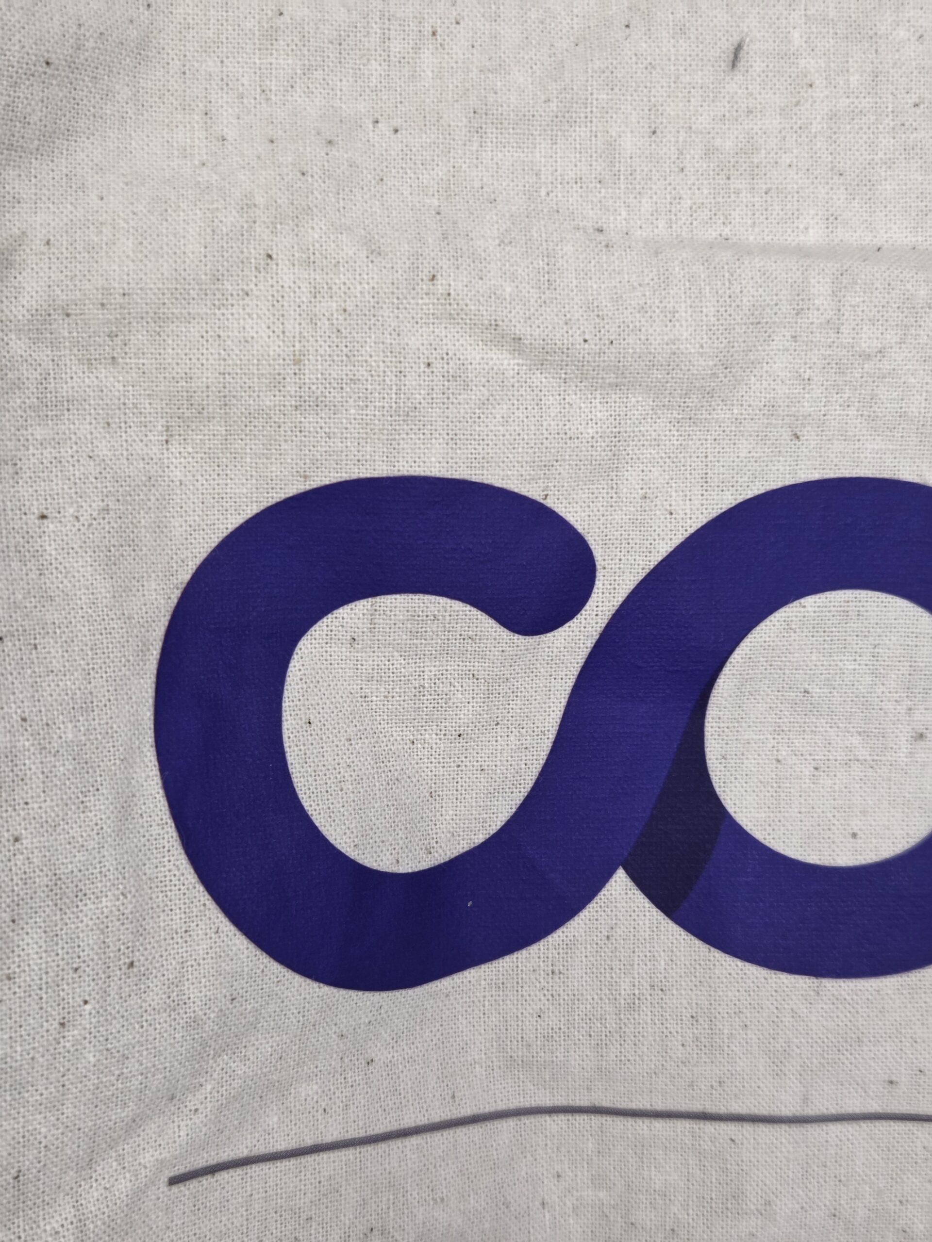 Close-up of a blue lowercase c printed on a textured cotton tote bag background.