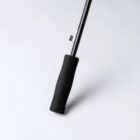 A close-up of a black foam handle on a metal walking stick against a light background.