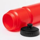 Red plastic bottle lying down with black screw cap placed beside its opening.
