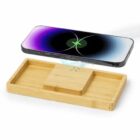 Smartphone wirelessly charging on a rectangular bamboo charging tray with compartments.