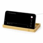Smartphone on a wooden stand, playing a video with charging cable connected.