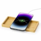 Smartphone charging wirelessly on a wooden charging pad with a cable attached.