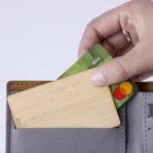 Hand placing a green debit card and a wooden card into a gray wallet.