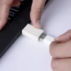 Hand plugging a white USB drive into a laptop USB port.