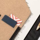 Close-up of a notebook, a card in a pocket, and a pencil on a black surface.