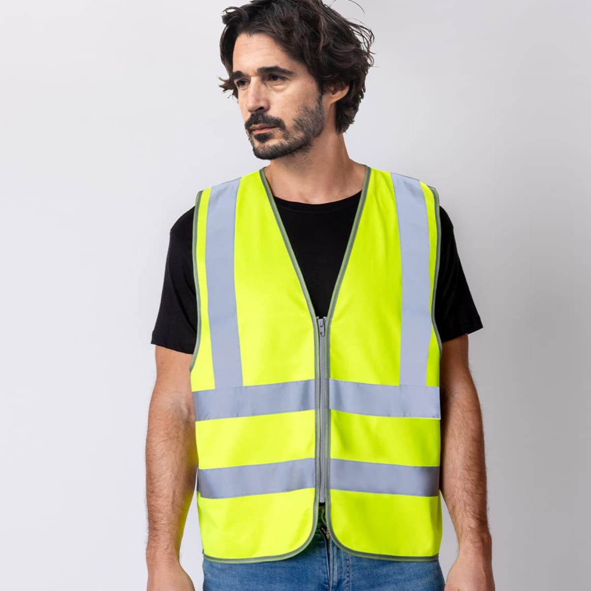Man wearing a neon yellow reflective safety vest over a black t-shirt and blue jeans.
