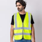 Man wearing a bright yellow reflective safety vest over a black shirt, standing against a gray wall.
