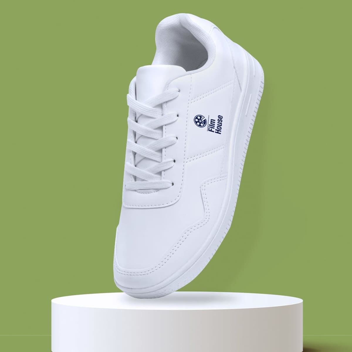 White sneaker with Film House logo, displayed on a white pedestal against a green background.