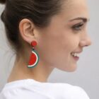 Woman smiling, wearing a watermelon-shaped earring, shown in profile against a light background.