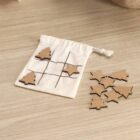 Tic-tac-toe game with wooden tree and star pieces on a cloth bag on a wooden table.