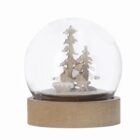 Glass snow globe with wooden trees inside, set on a round wooden base.