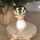 Wooden reindeer figurine with a white beard on a round wooden platform under a tree.