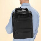 Man in blue shirt carrying a black rectangular backpack over one shoulder, seen from behind.