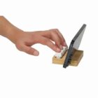 A hand typing on a small keyboard with a smartphone placed in a wooden stand.