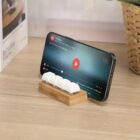 Smartphone on a wooden stand with white keycaps, displaying a video paused on screen.
