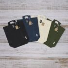 Four tote bags in black, navy, cream, and green laid out on a wooden surface.