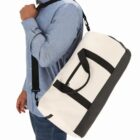 Person in blue shirt carrying a white and black duffel bag over their shoulder.