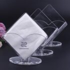 Clear napkin holders with white napkins, arranged in a row on a dark surface.