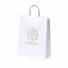 White paper shopping bag with handles and a gold leaf emblem design on the front.