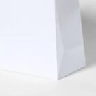 Close-up of the bottom corner of a plain white paper bag on a white surface.