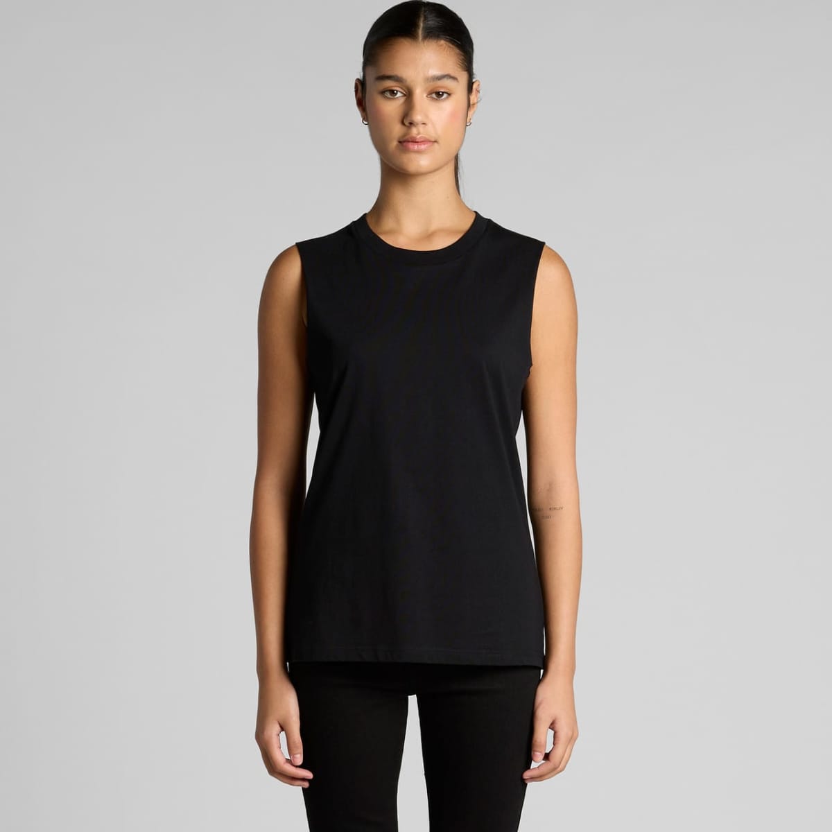 Woman in a sleeveless black top and black pants standing against a plain gray background.