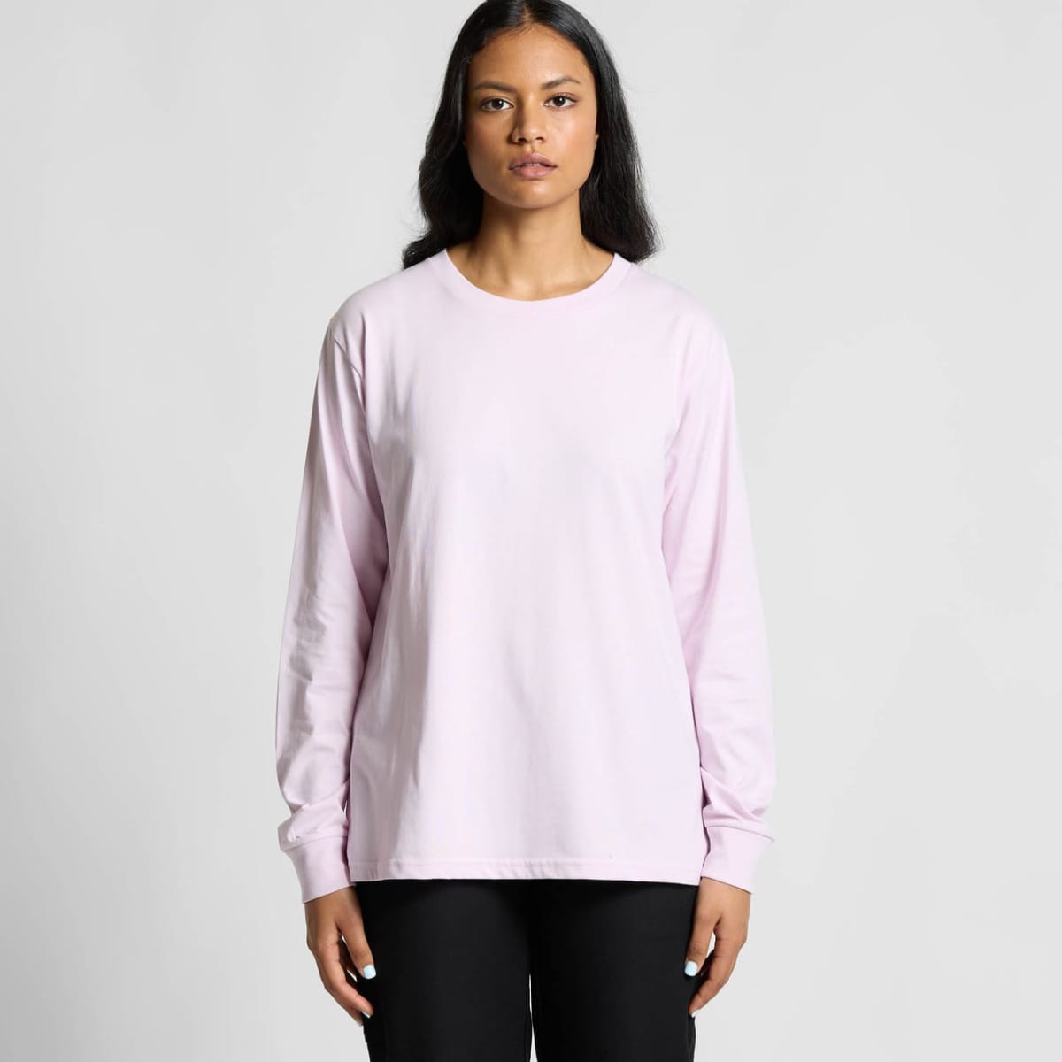 Woman in a plain light pink long-sleeve shirt stands facing forward against a plain background.