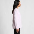 Woman in a light pink long-sleeve shirt and black pants standing in profile view.