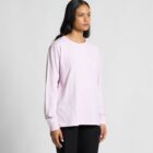 Woman in a light pink long-sleeve shirt and black pants standing against a gray background.