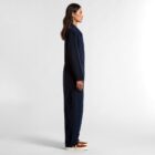 A person in a navy jumpsuit and brown sneakers stands in profile against a white background.