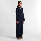 A woman in a navy blue coverall stands facing right against a plain white background.