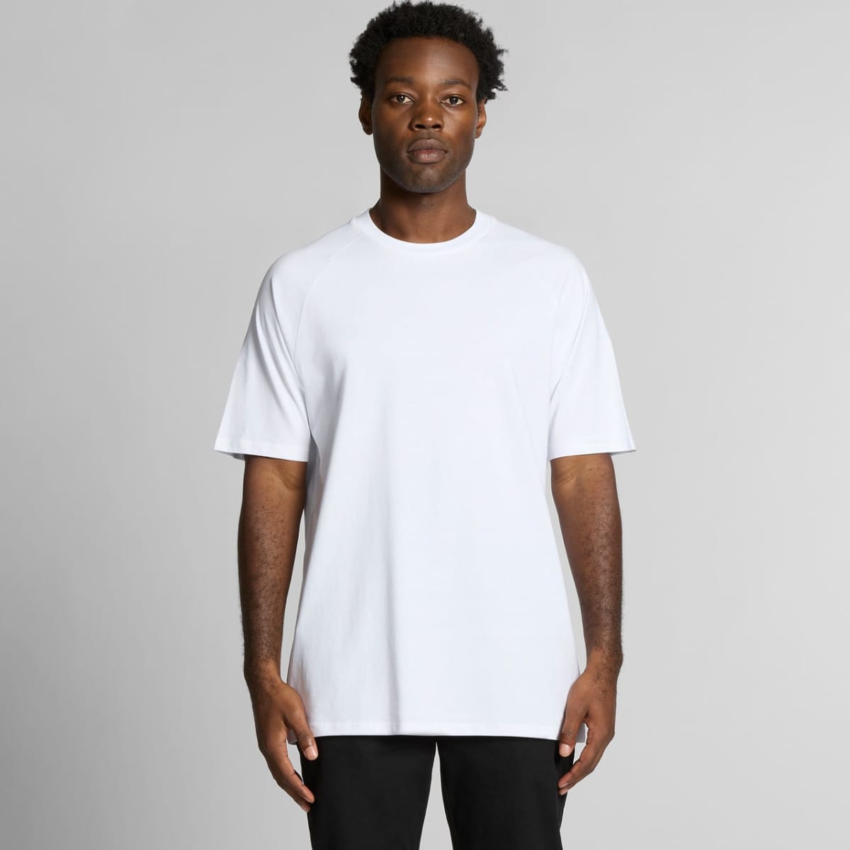 A man wearing a plain white T-shirt and black pants stands against a light gray background.
