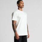Man with tattoos wearing a plain white t-shirt and black pants, standing against a gray background.