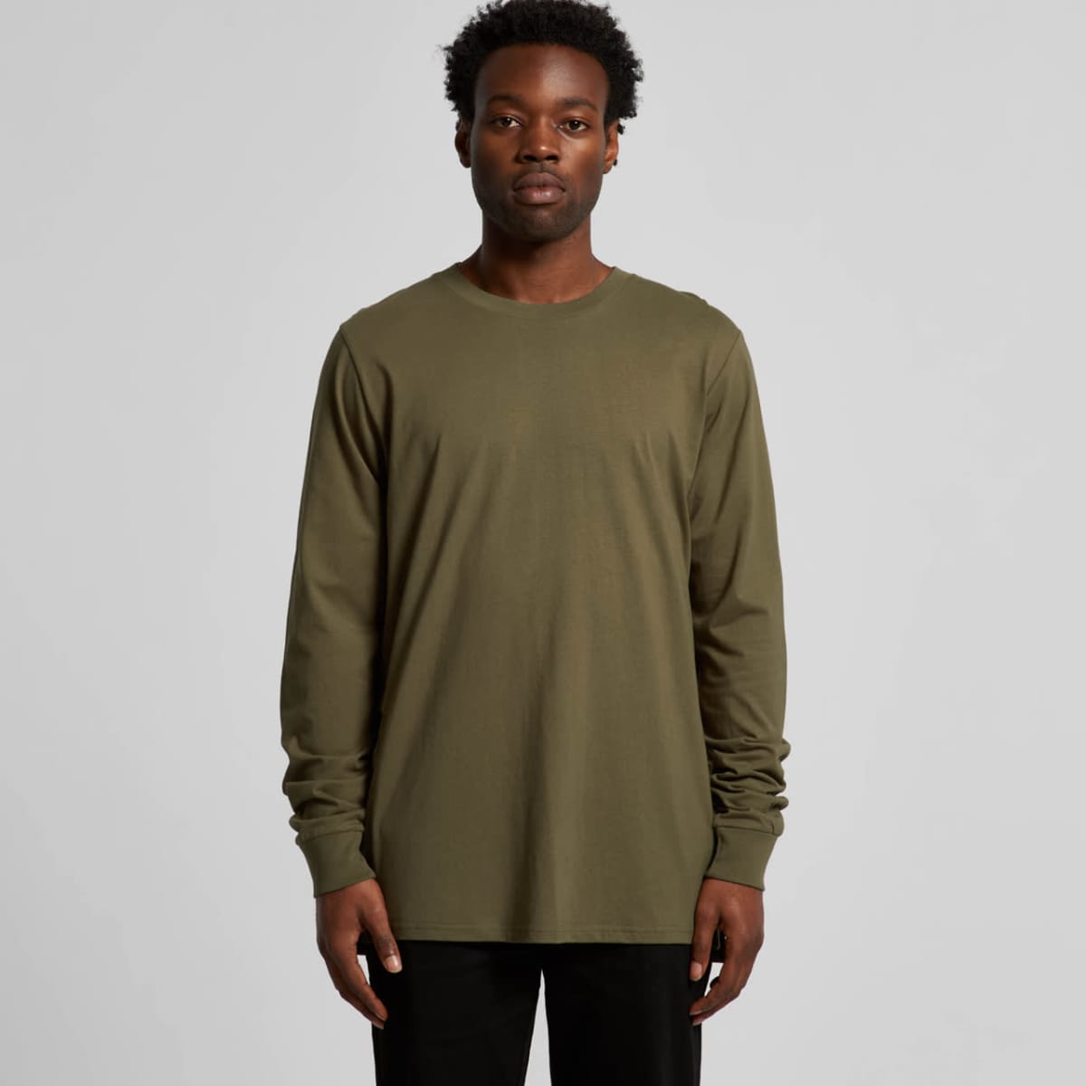 Man wearing an olive green long-sleeve shirt and black pants, standing against a gray background.
