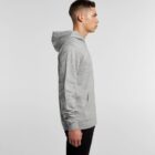 Man in a gray hoodie and black pants standing in profile against a plain background.