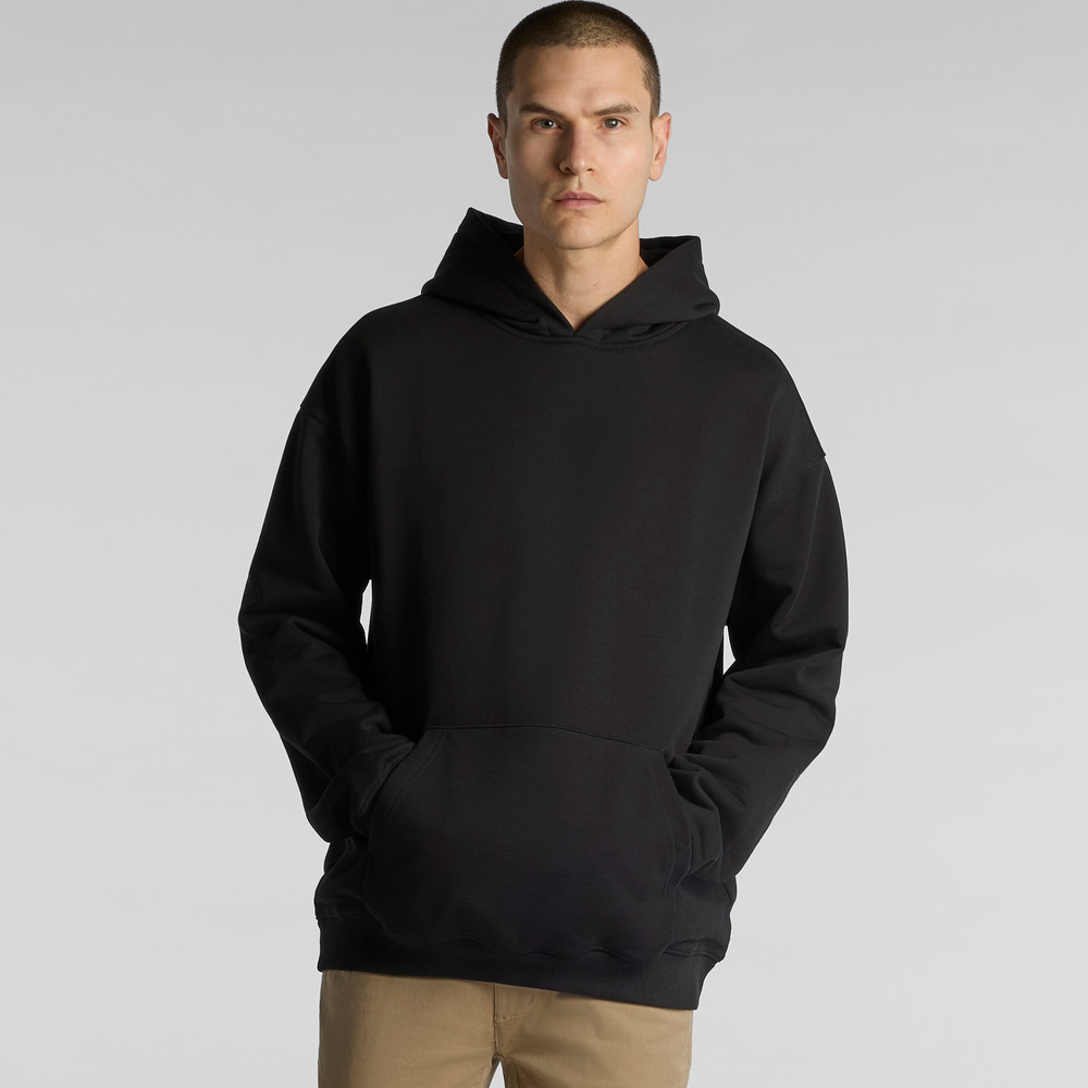 A person in a premium quality AS Colour MADE Hoodie and tan pants stands against a plain background.