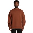Man wearing a brown oversized sweatshirt and black pants, standing against a white background.
