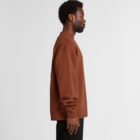 Man in a brown sweatshirt and black pants standing in profile against a plain background.