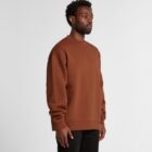 Man wearing a brown sweatshirt and black pants, standing against a plain light background.