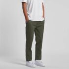 Man wearing olive green pants, white t-shirt, and white sneakers with hands in pockets.
