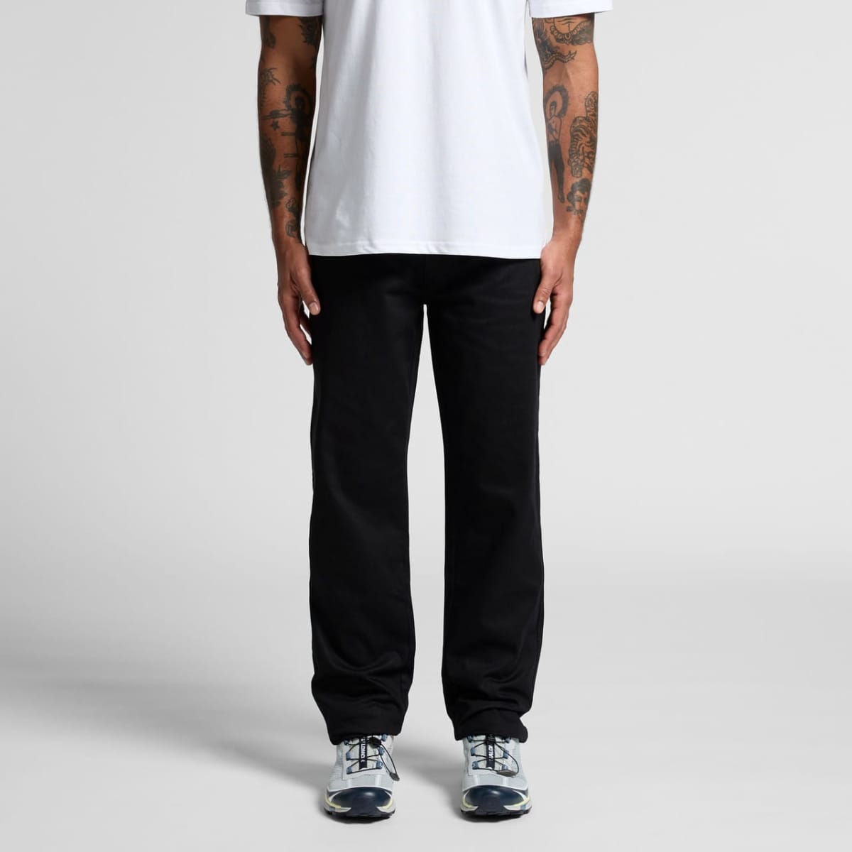 Person in white t-shirt, black pants, and sneakers standing against a plain background.